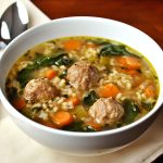 Italian wedding soup served in a rustic bowl with tender meatballs, fresh spinach, carrots, and tiny pasta in a savory broth, garnished with Parmesan cheese.