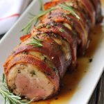 Juicy bacon-wrapped pork tenderloin sliced on a cutting board with a crispy, golden bacon exterior.