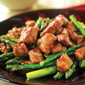 Pork and asparagus stir-fry with tender pork slices, crisp asparagus, and savory hoisin sauce served in a skillet, garnished with sesame seeds and green onions.
