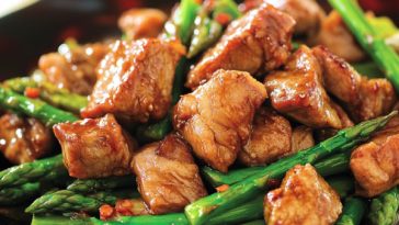 Pork and asparagus stir-fry with tender pork slices, crisp asparagus, and savory hoisin sauce served in a skillet, garnished with sesame seeds and green onions.