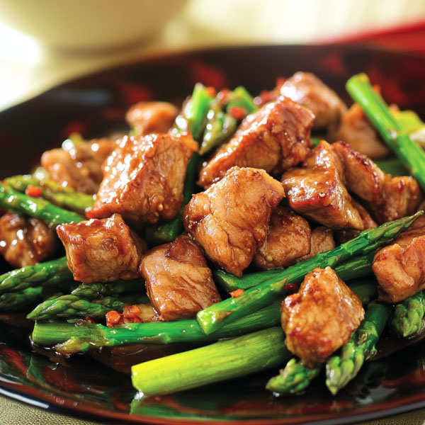 Pork and asparagus stir-fry with tender pork slices, crisp asparagus, and savory hoisin sauce served in a skillet, garnished with sesame seeds and green onions.