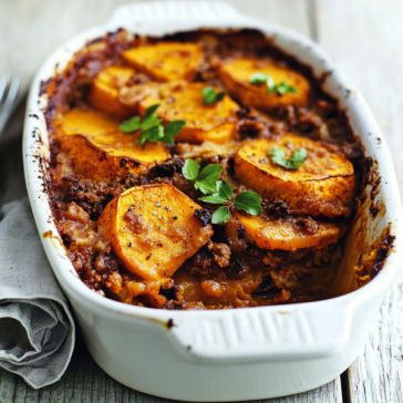 Golden butternut squash mince bake topped with melted cheese, baked in a casserole dish, garnished with fresh herbs.