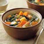 Winter-vegetable soup served in a rustic bowl, filled with carrots, parsnips, potatoes, kale, and beans in a hearty broth, garnished with fresh herbs.