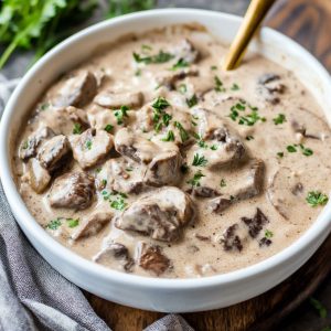 Slow Cooker Beef Stroganoff Stew Recipe with tender beef chunks, creamy sauce, mushrooms, and fresh herbs served over egg noodles.