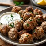 Greek meatballs (keftedes) served on a platter, golden brown and crispy, garnished with fresh parsley and lemon wedges, with tzatziki sauce on the side.