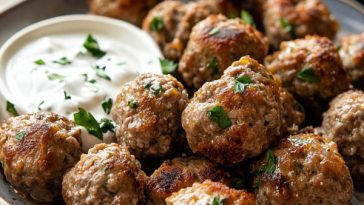 Greek meatballs (keftedes) served on a platter, golden brown and crispy, garnished with fresh parsley and lemon wedges, with tzatziki sauce on the side.
