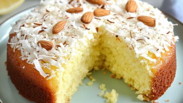 Easy Lemon Coconut Almond Cake Recipe with golden cake topped with toasted almonds, shredded coconut, and lemon glaze on a serving plate.