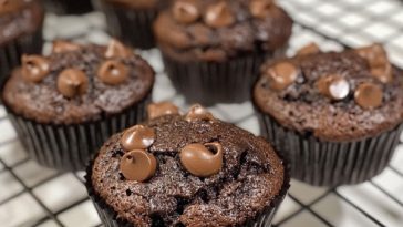 Freshly baked chocolate muffins with a rich cocoa flavor, topped with chocolate chips and served on a rustic plate.