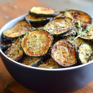 Crispy baked zucchini chips seasoned with herbs and Parmesan, served golden brown on a tray.