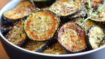 Crispy baked zucchini chips seasoned with herbs and Parmesan, served golden brown on a tray.