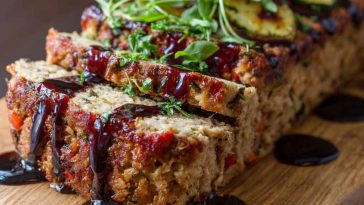 Vegetable meatloaf topped with balsamic glaze, sliced and served on a platter with fresh herbs, showcasing a hearty and colorful loaf.