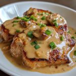 Smothered pork chops cooked in a rich onion gravy, served with mashed potatoes and garnished with fresh herbs on a rustic plate.