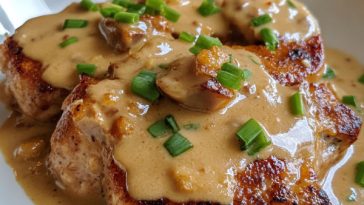 Smothered pork chops cooked in a rich onion gravy, served with mashed potatoes and garnished with fresh herbs on a rustic plate.