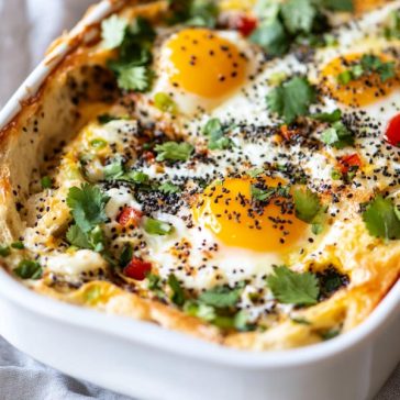 Everything bagel egg bake served in a casserole dish, layered with bagel pieces, eggs, cheese, and seasonings, baked golden brown and garnished with fresh herbs.