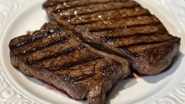 Perfectly grilled steak with charred grill marks, juicy center, and fresh herbs served on a wooden board with sides.