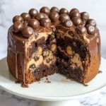 Maltesers marble cake with swirls of chocolate and vanilla sponge, topped with creamy frosting and crunchy Maltesers candy pieces.