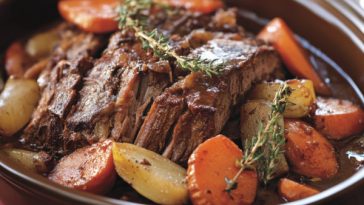 Tender company pot roast served with carrots, potatoes, and onions in a rich gravy, garnished with fresh herbs for a hearty family-style dinner.