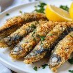 Crispy Italian crusted sardines with golden herb coating served on a plate with lemon wedges.