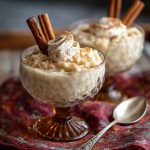 “A creamy rice pudding topped with ground cinnamon and garnished with a cinnamon stick in a serving bowl.”