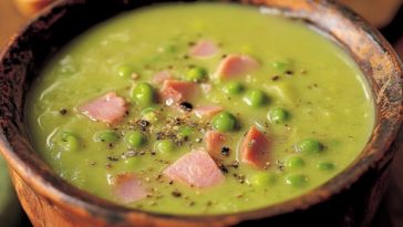 Warm bowl of pea and ham soup with tender ham chunks, green peas, carrots, and herbs, served with crusty bread.