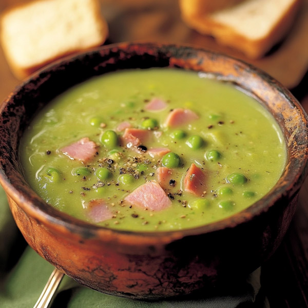 Warm bowl of pea and ham soup with tender ham chunks, green peas, carrots, and herbs, served with crusty bread.