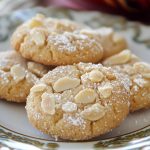 “Golden Cretan almond cookies arranged on a plate, lightly dusted with powdered sugar.”