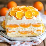 Orange dreamsicle icebox cake layered with vanilla wafers, creamy orange filling, and whipped topping, chilled in a baking dish and garnished with orange slices.
