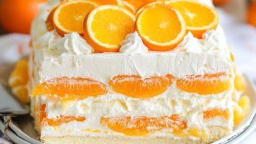 Orange dreamsicle icebox cake layered with vanilla wafers, creamy orange filling, and whipped topping, chilled in a baking dish and garnished with orange slices.