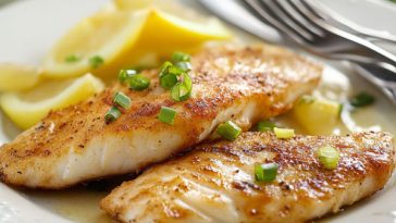 Golden pan‑fried fish fillets with lemon wedges and fresh herbs served on a rustic plate