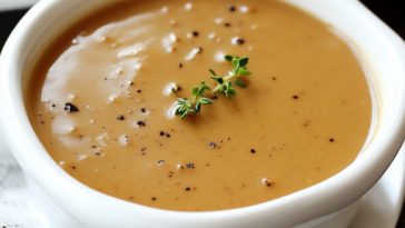 Rich turkey gravy served in a gravy boat, golden brown and silky smooth, poured over roasted turkey slices with herbs.