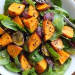 Roasted sweet potato salad with honey lemon dressing, tossed with fresh greens, cranberries, feta cheese, and toasted pecans, served in a rustic bowl.