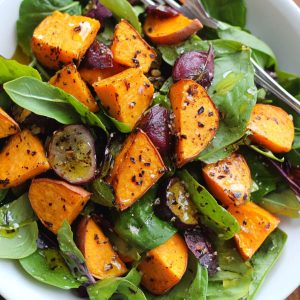 Roasted sweet potato salad with honey lemon dressing, tossed with fresh greens, cranberries, feta cheese, and toasted pecans, served in a rustic bowl.