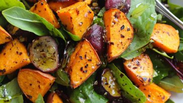Roasted sweet potato salad with honey lemon dressing, tossed with fresh greens, cranberries, feta cheese, and toasted pecans, served in a rustic bowl.