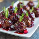 Savory cranberry meatballs glazed with sweet cranberry sauce, garnished with parsley, and served in a festive dish.