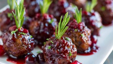 Savory cranberry meatballs glazed with sweet cranberry sauce, garnished with parsley, and served in a festive dish.