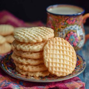 Golden vanilla wafer cookies stacked neatly on a plate, with a light, crisp texture and sweet aroma.