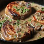 Juicy smothered pork chops covered in rich onion gravy, served with mashed potatoes and fresh herbs.