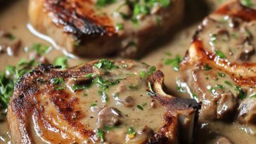 Juicy smothered pork chops covered in rich onion gravy, served with mashed potatoes and fresh herbs.