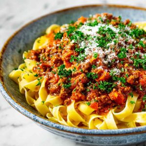 Classic Marcella Hazan’s Bolognese sauce simmering in a pot with ground beef, tomatoes, milk, and aromatic vegetables.