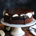 Rich chocolate Guinness cake topped with creamy frosting, served on a rustic cake stand with a slice cut out.