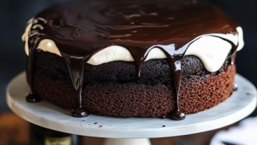 Rich chocolate Guinness cake topped with creamy frosting, served on a rustic cake stand with a slice cut out.
