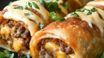 Golden, crispy cheeseburger eggrolls filled with seasoned beef, melted cheese, and pickles, served with dipping sauce.