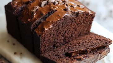"A loaf of rich brownie bread sliced to reveal its fudgy, chocolatey texture, topped with a dusting of cocoa powder."