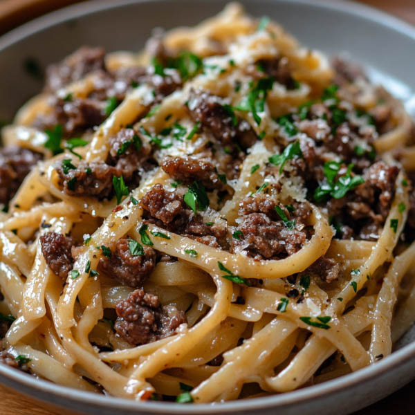 “A bowl of garlic beef pasta with tender beef strips, spaghetti coated in garlic butter sauce, and parsley garnish.”