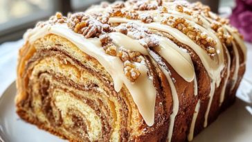A golden, swirled honey babka loaf topped with creamy frosting, sliced to reveal its rich layers.