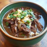 “A steaming bowl of French onion beef short rib soup topped with melted cheese and toasted bread.”