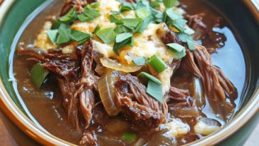 “A steaming bowl of French onion beef short rib soup topped with melted cheese and toasted bread.”