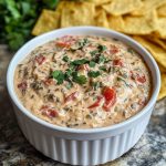 A creamy bowl of boat dip (Rotel ranch dip) topped with shredded cheese and served with tortilla chips.