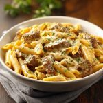 "Creamy Velveeta beef stroganoff with penne pasta served in a bowl, topped with parsley and melted cheese."