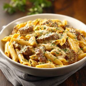 "Creamy Velveeta beef stroganoff with penne pasta served in a bowl, topped with parsley and melted cheese."
